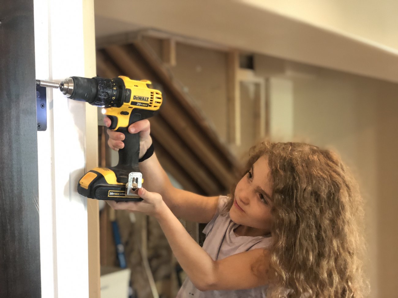 A young girl driving a screw into a door frame with a cordless drill