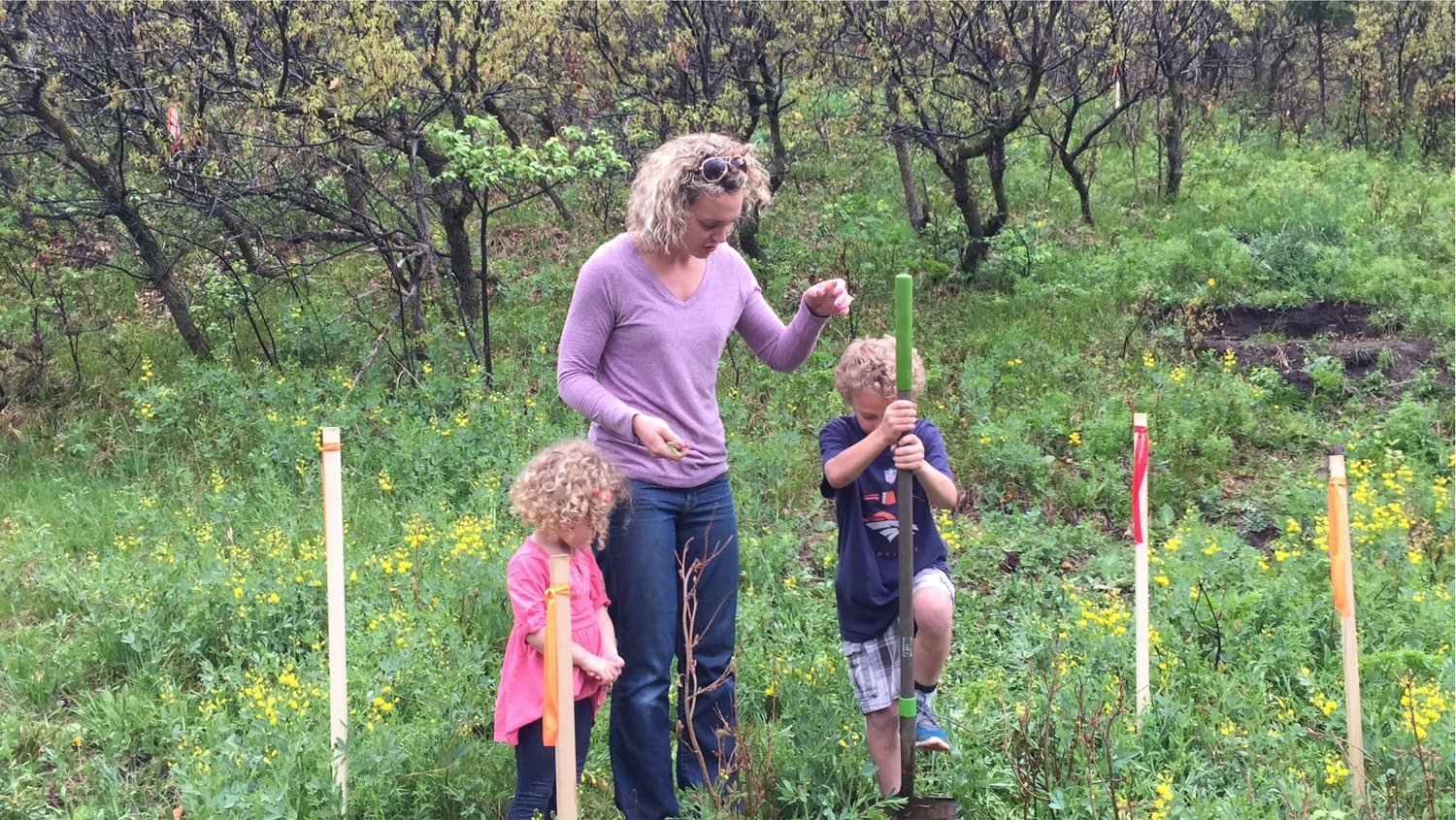 A family standing on a freshly staked building site among burnt scrub oak, red rock formations beyond