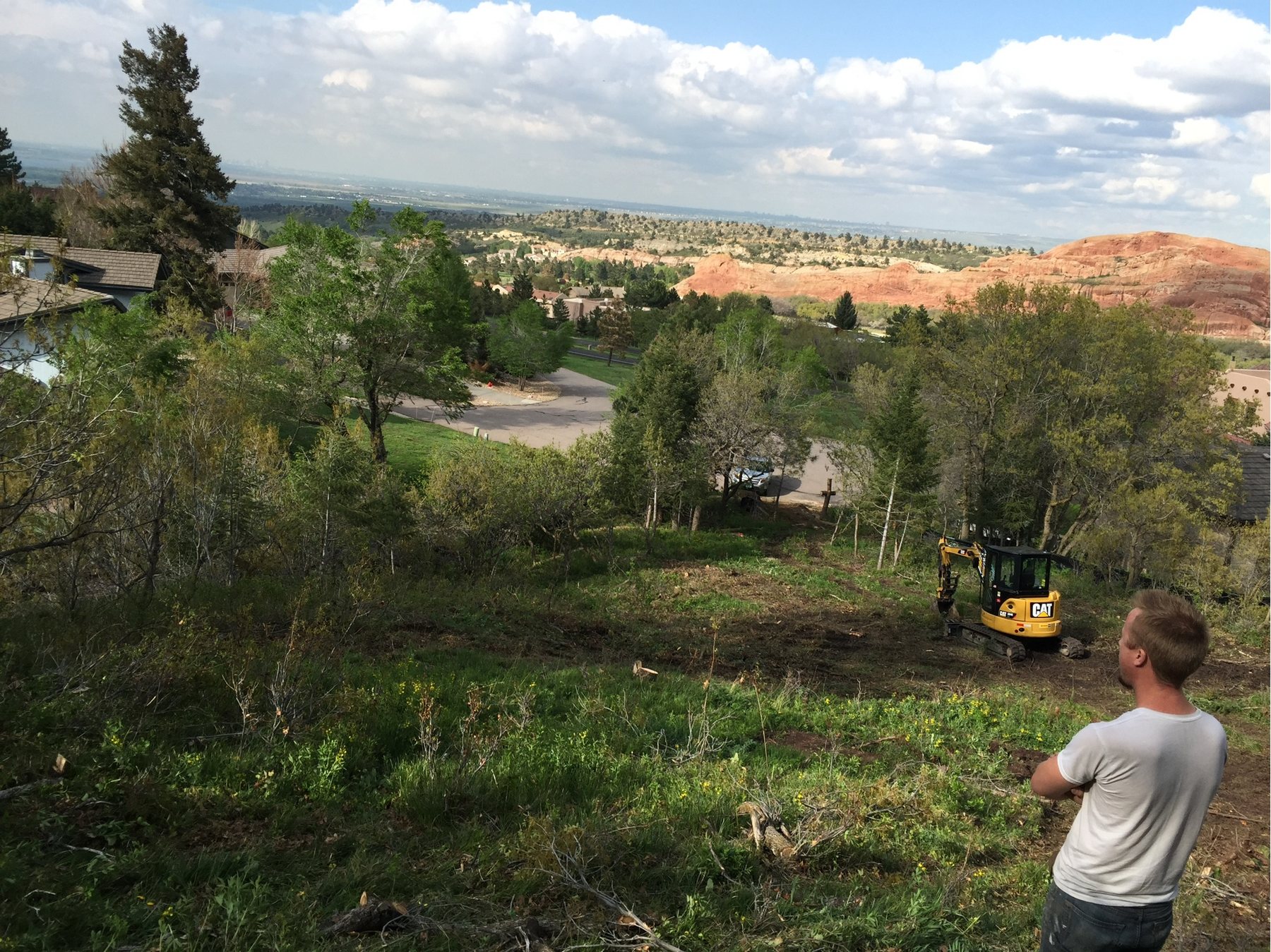 A cleared building envelope on a sloping lot, red rock formations in the distance