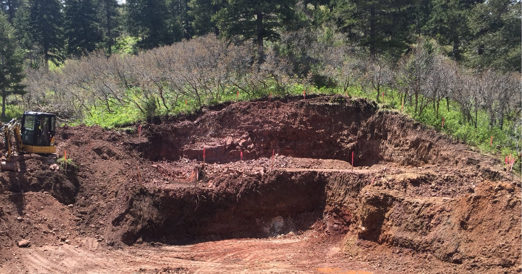 Open excavation cut into a sloping site, benched walls of red soil