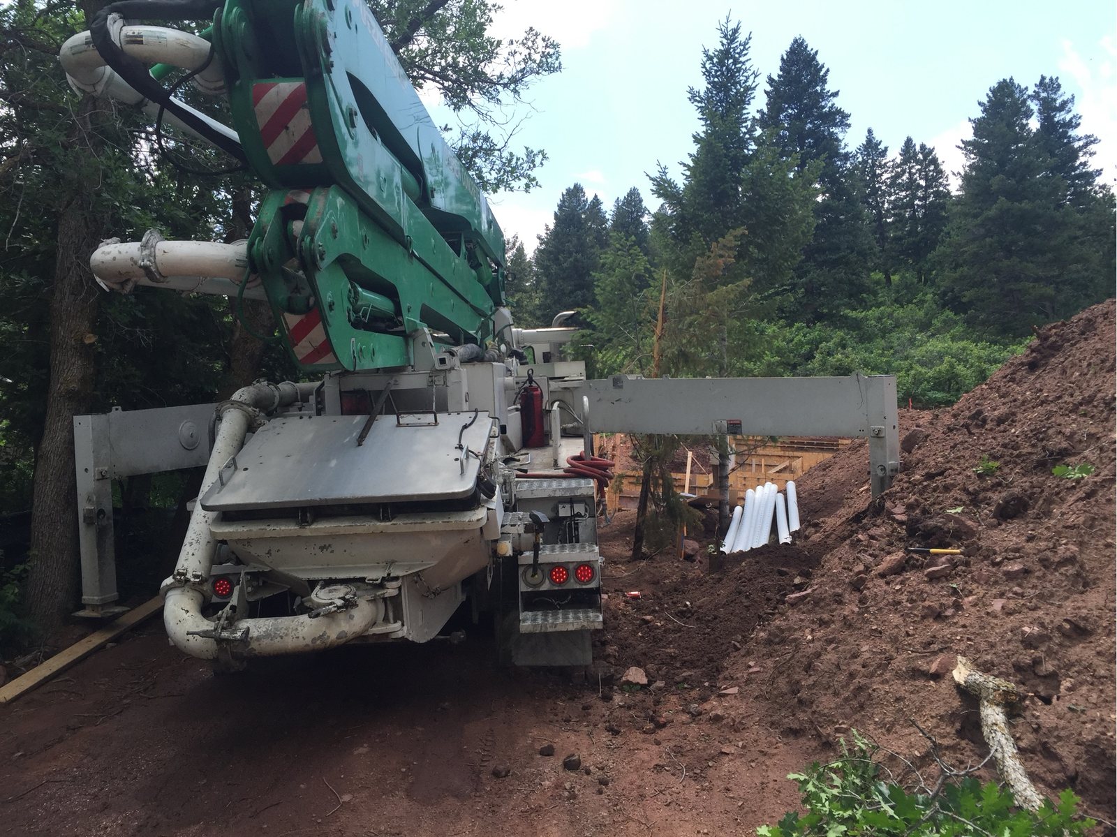 Concrete pump truck positioned on narrow wooded access with the boom extended