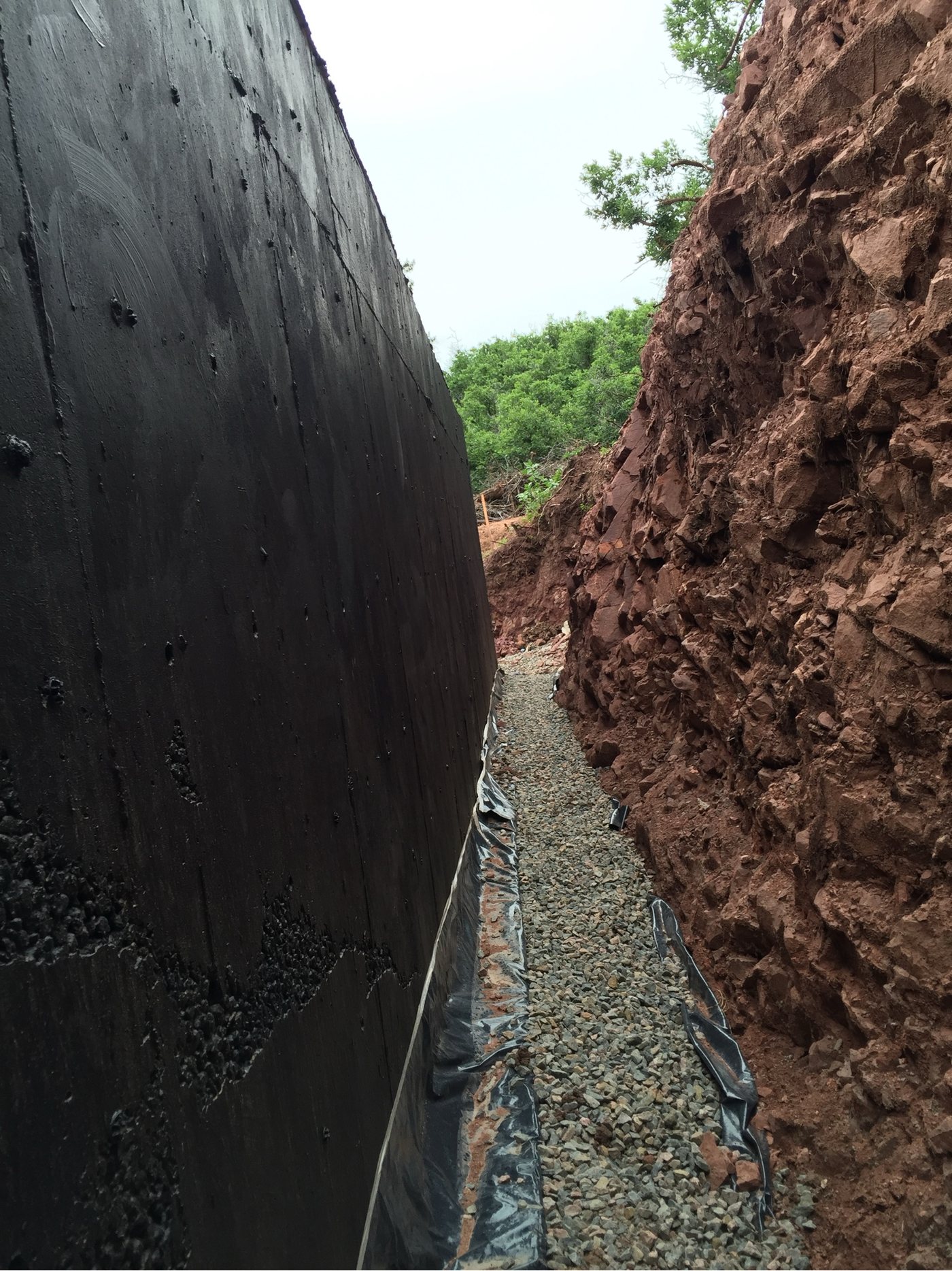 Foundation wall coated in damproofing with free-draining gravel placed against it