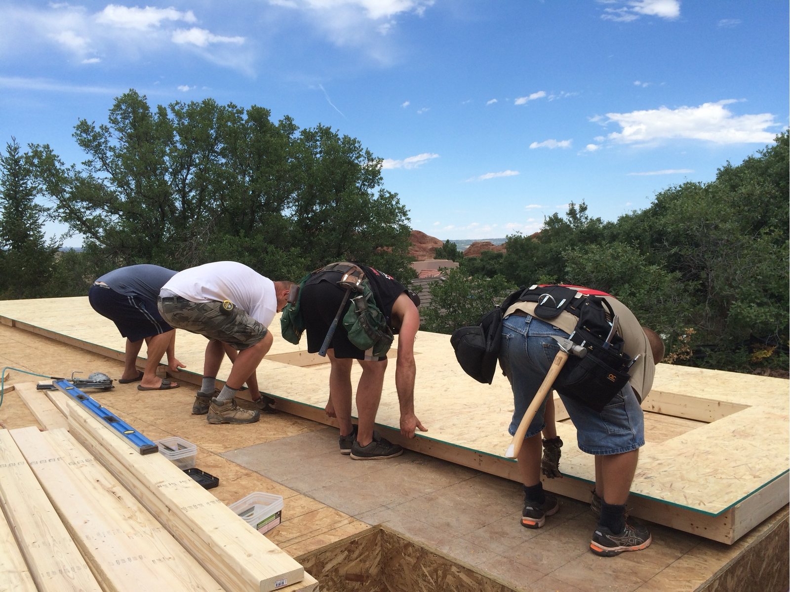 Four workers bent over a framed wall lying flat on the deck, preparing to lift