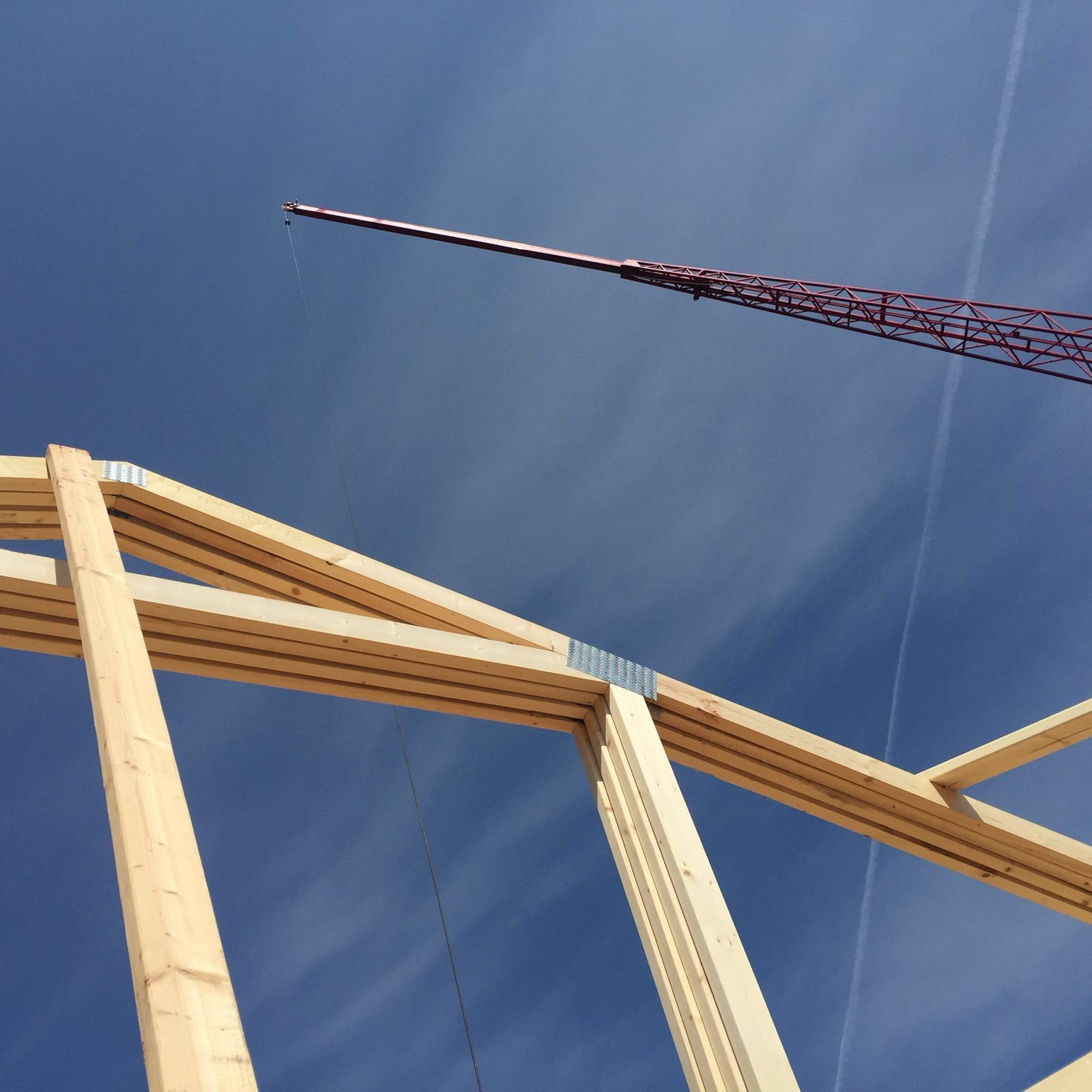Ridge beam being set by crane, seen from below through the truss.