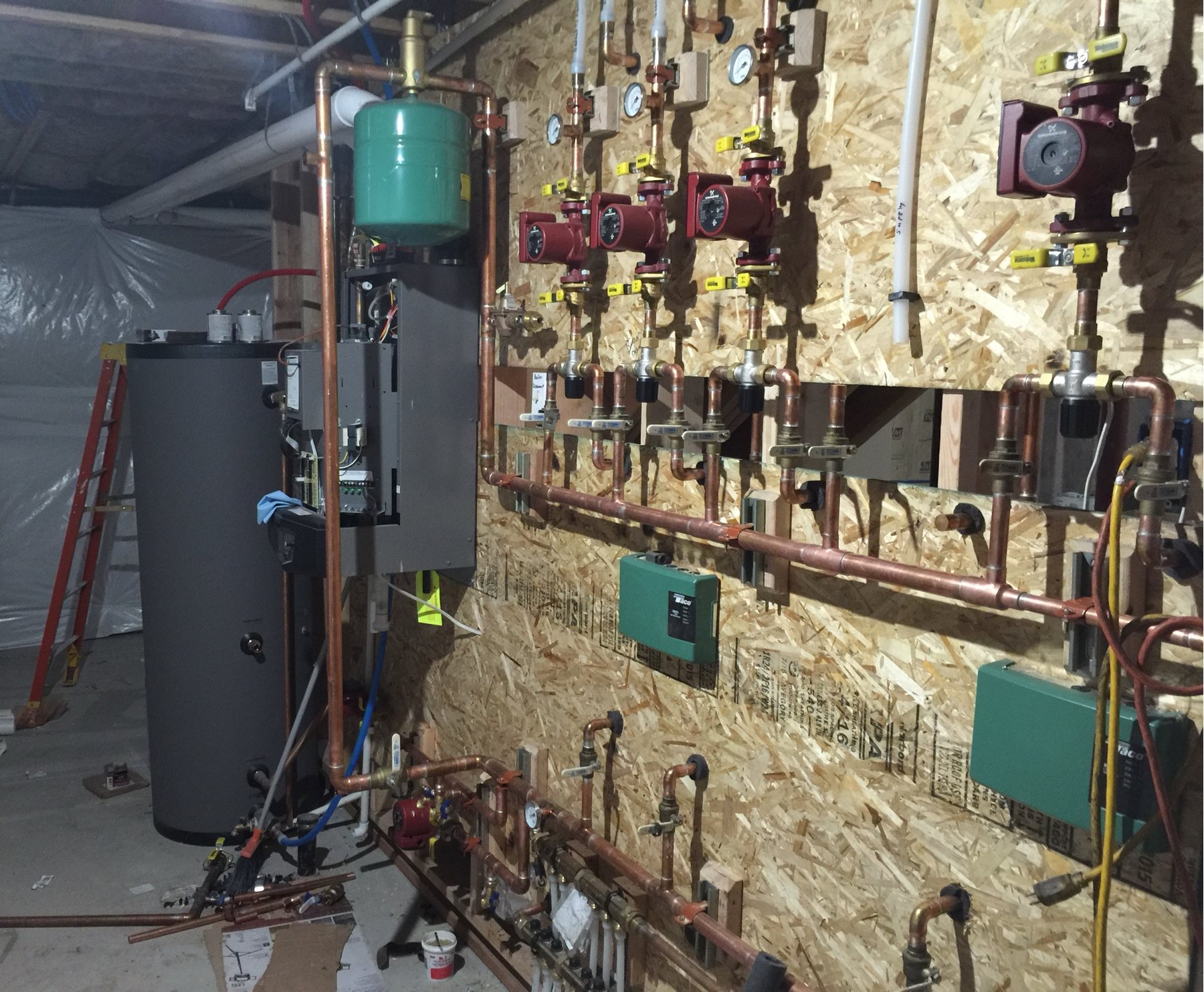 A finished mechanical room with labelled copper manifolds, boiler and radiant zones.