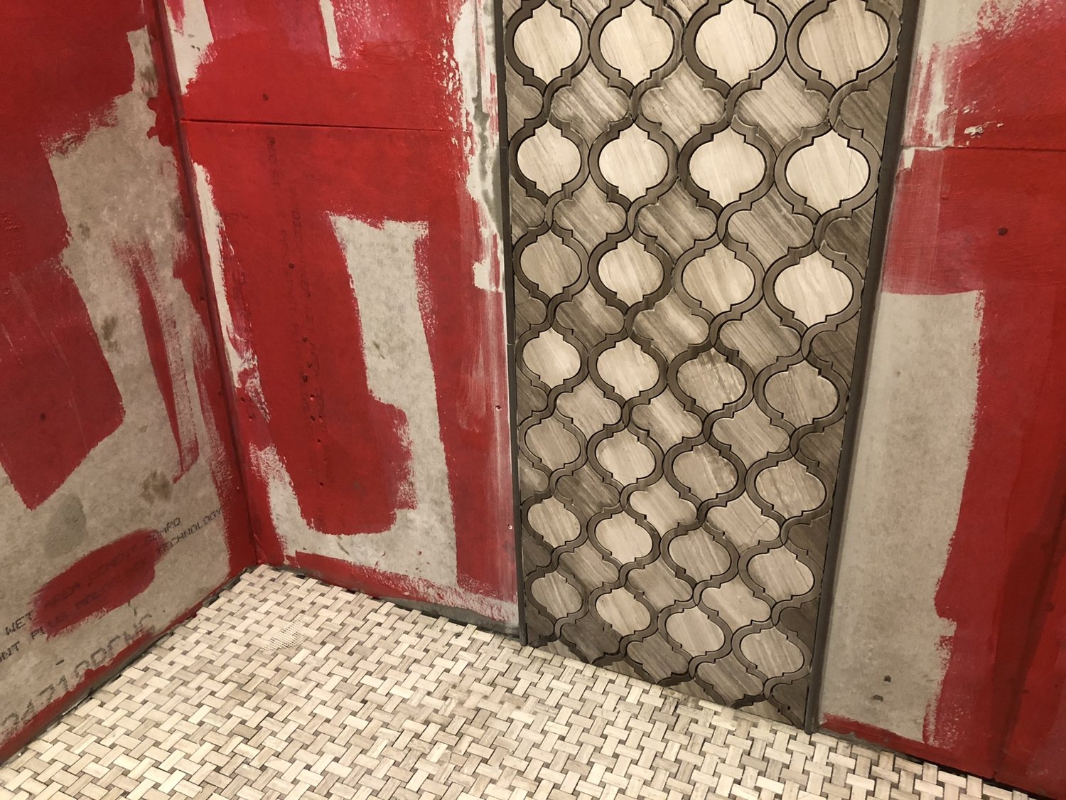 Shower walls coated in red waterproofing membrane with a mortar-bed pan and the first course of tile set.