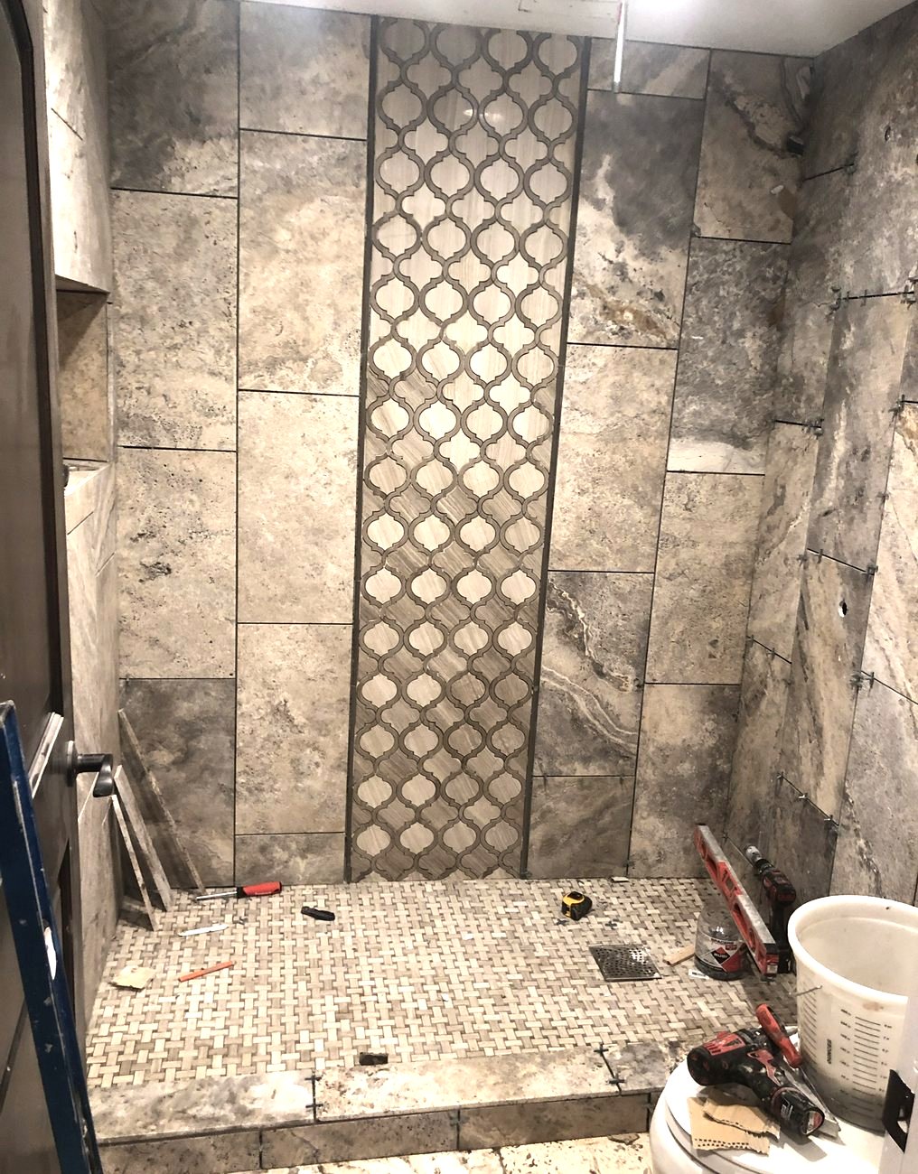The same shower finished in honed stone tile with a patterned inset band.
