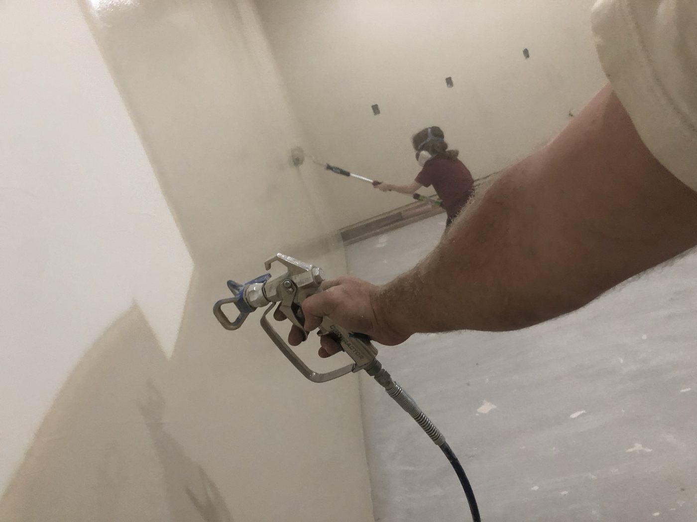 Close view of a hand running a sprayer along a finished drywall corner