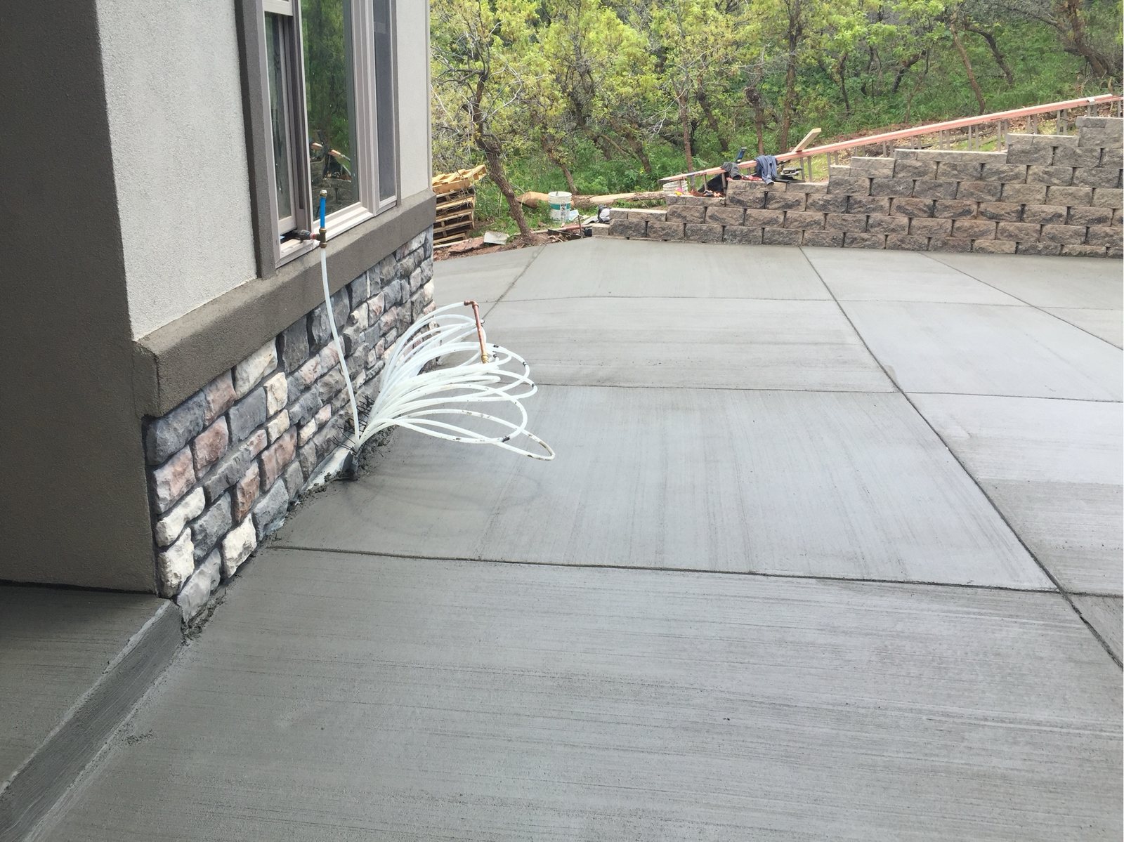 Stone veneer carried down to grade beside a broom-finished concrete drive and a stacked retaining wall