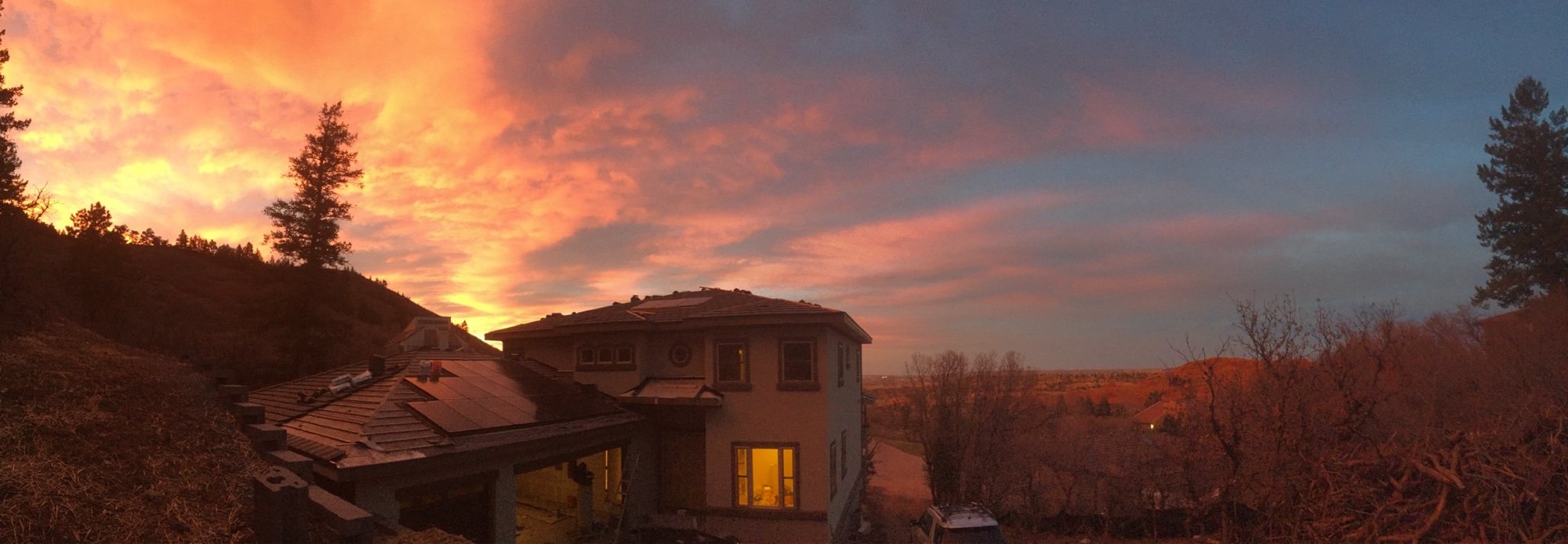 A finished custom home at dusk, warm light in every window, Front Range foothills behind it.