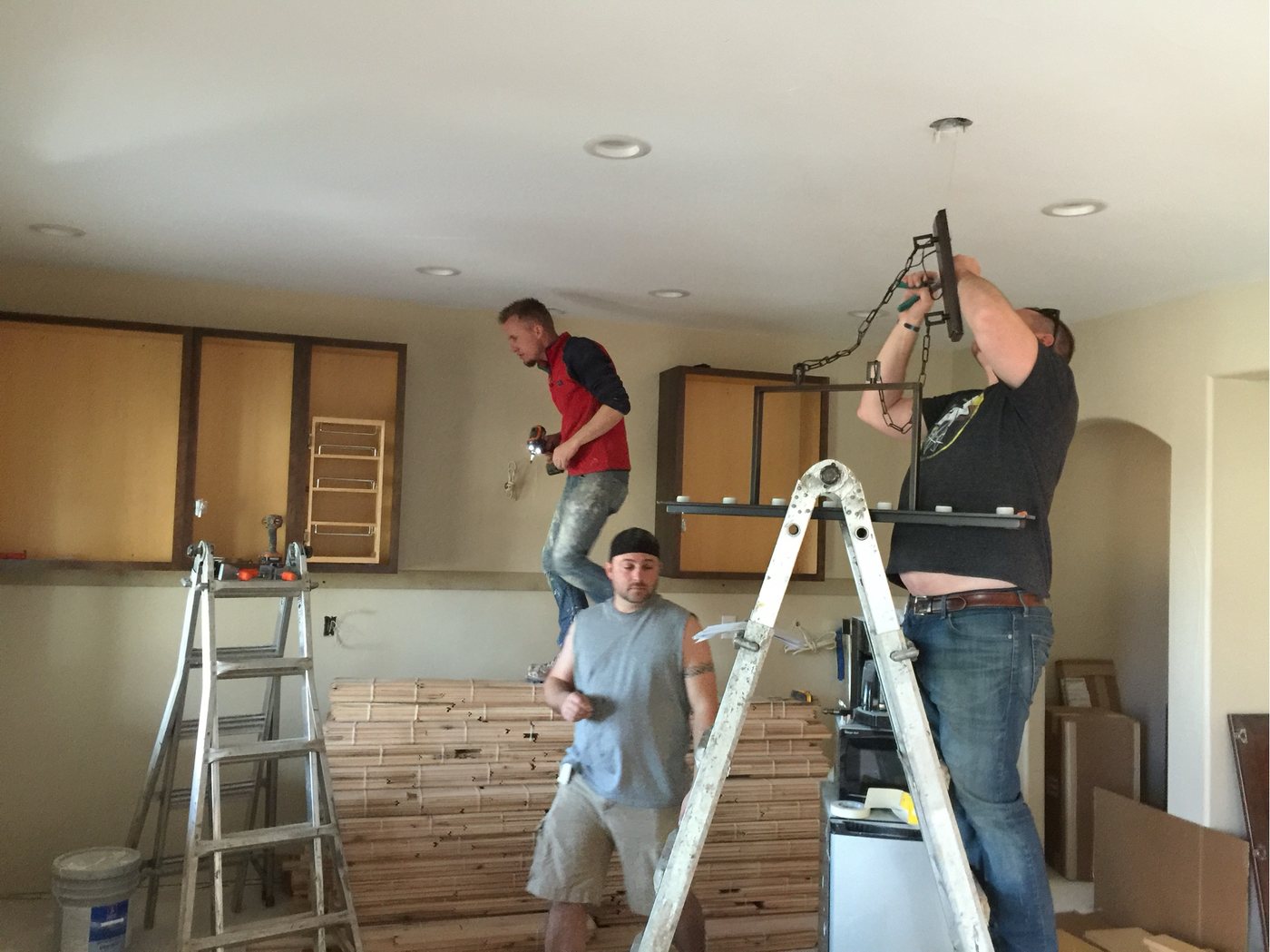 Three tradespeople setting a light fixture while plank flooring acclimates stacked on the floor below
